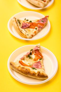 Takeaway and delivery. Three pieces of pizza in disposable plastic plates on a yellow background. Lunch for a group of friends. Vertical view
