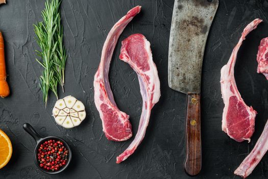 Raw lamb chops or mutton cuts set, with ingredients carrot orange, herbs, on black stone background, top view flat lay