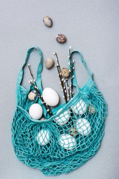 Happy Easter. Chicken and quail eggs falling into a blue mesh bag with pussy willow branches on a gray background