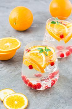 Hard seltzer cocktail with orange, cranberry and mint in glasses and cut oranges on the table. Alcoholic highly carbonated drink. Vertical view