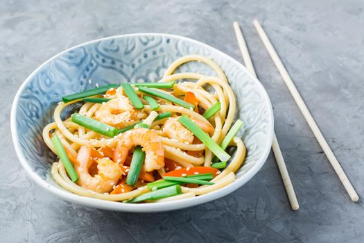 Udon and wok noodles with prawns, peppers and onions in a plate and chopsticks on the table. Chinese food