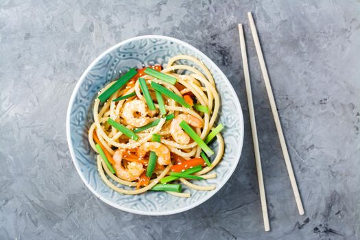 Udon and wok noodles with prawns, peppers and onions in a plate and chopsticks on the table. Chinese food. Top view