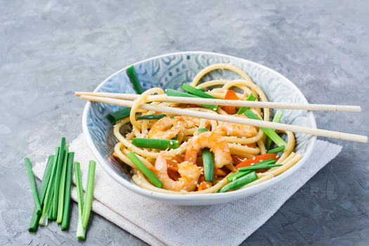 Ready to eat udon and wok noodles with prawns, peppers and onions in a plate and chopsticks on the table. Chinese food