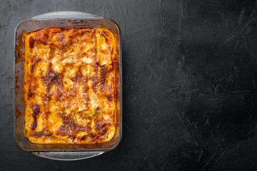 Traditional lasagna made with minced beef bolognese sauce topped with basil leafs set, in baking tray, on black stone background, top view, flat lay, with copy space for text