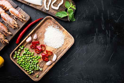 Traditional valenciana paella seafood ingredients with prawns, mussels, rice and spices on black concrete surface, flat lay with copy space, food photo.
