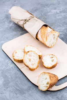 Fresh baguette in wrapping paper cut into pieces on a cutting board on a table. Vertical view