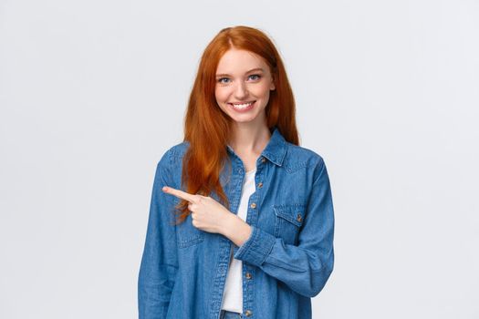 Here what need. Cheerful redhead woman in denim shirt, pointing finger left copy space, smiling recommend good product, review service, indicating website, standing white background.