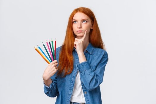 Thoughtful and focused, serious-looking determined redhead female student, teenager want draw something interesting, holding colored pencils look up thinking, pondering ideas.