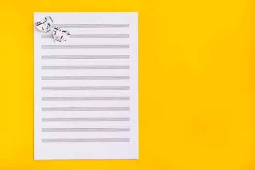 Blank sheet music and hearts cut from music text on yellow background. Top view. Copy space
