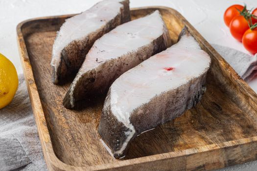 Raw steak of white fish set, with ingredients and rosemary herbs, on white stone table background