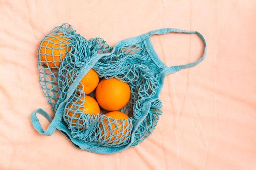 Fresh oranges in a mesh bag on a fabric background. Zero waste