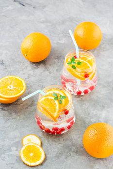 Hard seltzer cocktail with orange, cranberry and mint in glasses and cut oranges on the table. Alcoholic beverage. Vertical view