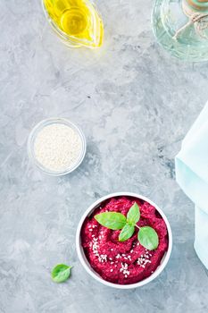 Homemade baked beetroot hummus in a bowl with sesame seeds and basil on the table. Top and vertical view