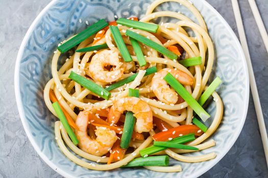 Udon and wok noodles with prawns, peppers and onions in a plate and chopsticks on the table. Chinese food. Top view. Close-up