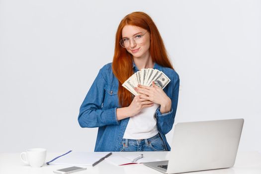 Girl loves money, feeling warmth of cash in hands, standing silly and delighted, received paycheck and grinning, going shopping online, making internet order, standing near laptop, white background.
