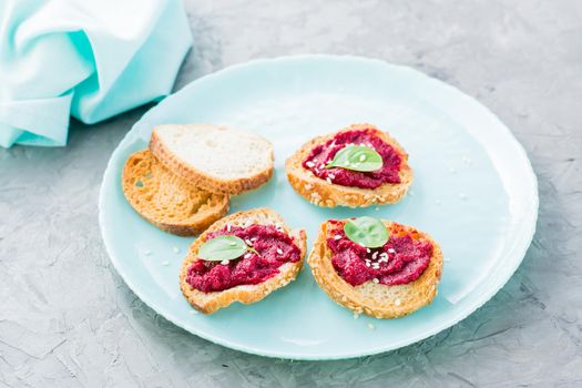 Homemade bruschetta with beetroot hummus on small baked baguette toast on a plate on the table. Close-up