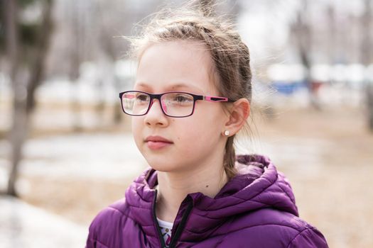 Young attractive serious girl in glasses in a city park in early spring looks into the distance
