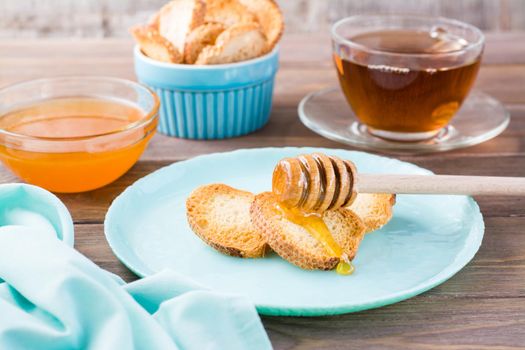 Small baked baguette toast with hot honey on a plate on a wooden table. Homemade tea