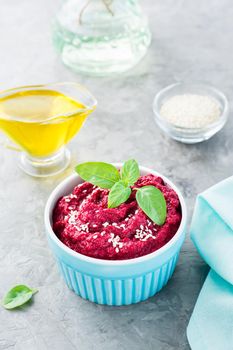 Baked beet hummus in a bowl with sesame seeds and basil on the table. Vertical view