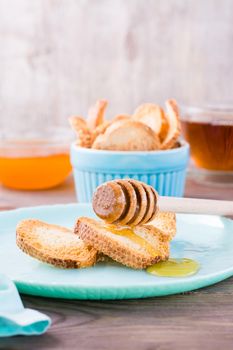 Small baked baguette toast with hot honey on a plate on a wooden table. Homemade tea. Vertical view. Close-up