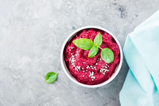 Homemade baked beetroot hummus in a bowl with sesame seeds and basil on the table. Close-up. Top view