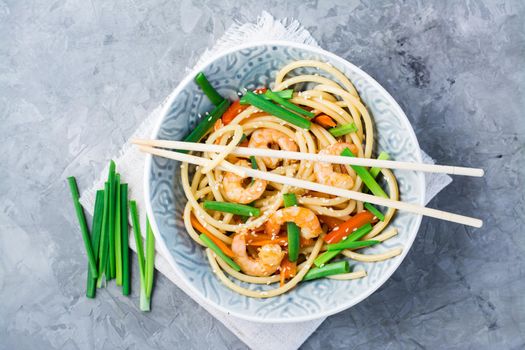 Ready to eat udon and wok noodles with prawns, peppers and onions in a plate and chopsticks on the table. Chinese food. Top view