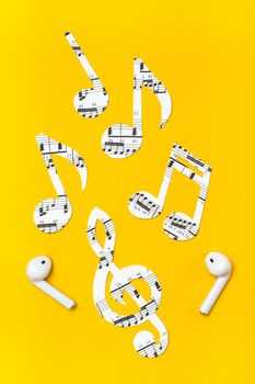 Wireless headphones and music notes cut from paper on a yellow background. Music imitation concept. Vertical view