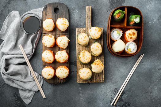 Baked sushi maki rolls with salmon, crab, cucumber, avocado, flying fish roe and spicy sauce set, on gray stone background, top view flat lay