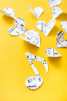 Musical notes, clef and hearts cut from paper with musical text on yellow background. Vertical view