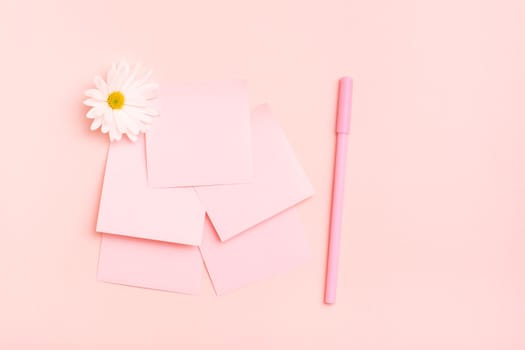 The concept is pink. Blank square small writing sheets, chrysanthemum and a pen on a pink background. Top view