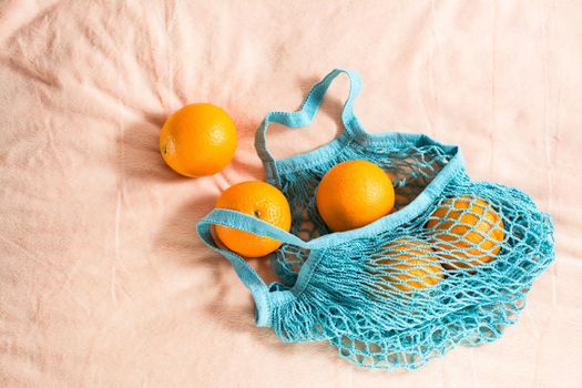 Fresh oranges in a mesh bag on a fabric background. Zero waste. Hard light