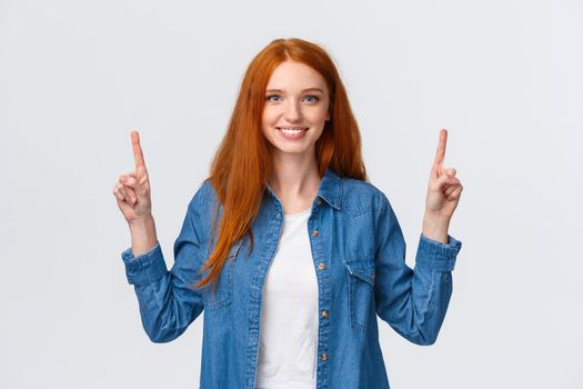 Waist-up portrait confident happy, alluring redhead female in denim shirt, pointing fingers up, smiling broadly, recommend company service, showing promo with product, white background.