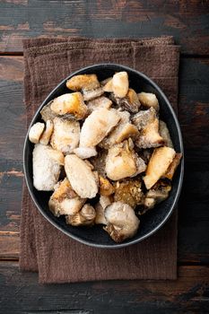Frozen wild mushrooms set, in bowl, on old dark wooden table background, top view flat lay