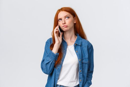 Perplexed over decisions. Unsure cute redhead woman order take-away in favorite restaurant, calling someone on phone, look thoughtful, thinking, pondering answer while talking, holding smartphone.