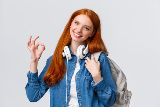 Education, scholarship and university concept. Lovely teenage girl picked best choice where study, want go abroad receive bachelor degree, holding backpack make okay sign and smiling.