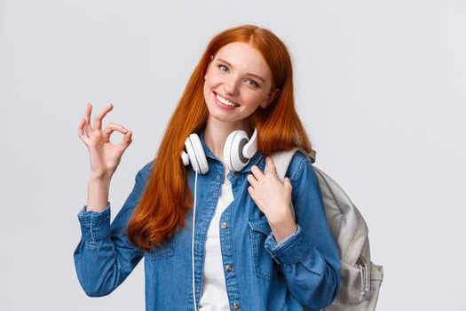 Education, scholarship and university concept. Lovely teenage girl picked best choice where study, want go abroad receive bachelor degree, holding backpack make okay sign and smiling.