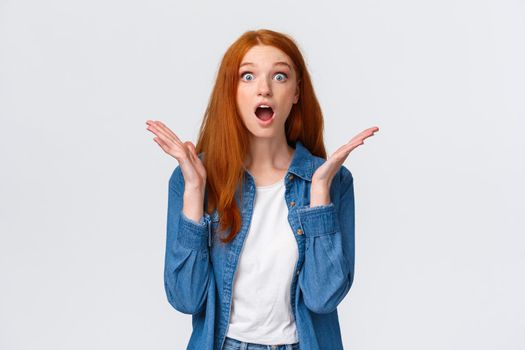 Surprised speechless redhead female learn excellent news, cant believe dream come true, staring camera drop jaw, gasping and raise hands sideways amazed, white background.