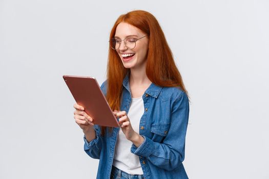 Waist-up porrtrait happy cheerful redhead girlfriend talking to partner using internet video-call service, laughing happily, having fun, smiling at gadget camera, standing white background.