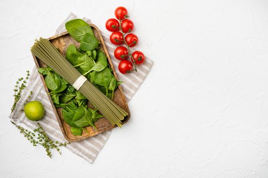 Green colored spaghetti raw dry spinach set, on white stone table background, top view flat lay, with copy space for text