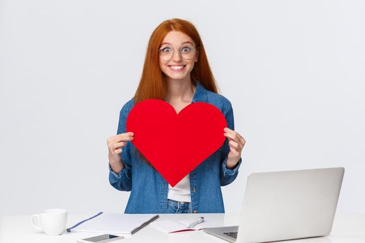 Cheerful and excited cute girlfriend with red hair, cant wait give big red valentines heart to boyfriend, showing sympathy, confess in love, celebrating lovers day, standing white background.