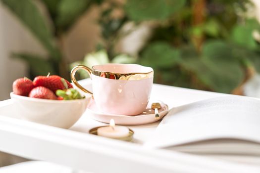 Breakfast in bed. Heart shaped white plate with fresh strawberries, cup of coffee, book and plants flowers. Still life composition. Mother, Valentine day concept.