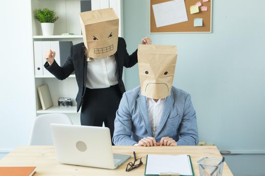 Business, emotions and people concept - Two angry and exhausted workers at working place. People wearing the packages on their heads with pictured emotions.