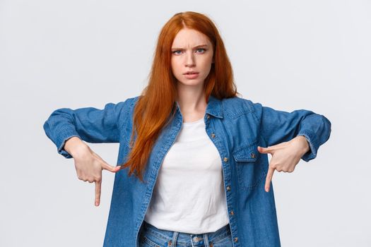 Mad and disturbed, questioned redhead woman waiting answer on question, pointing fingers down, frowning angry and distressed, cat made mess while she was at work, scolding over white background.