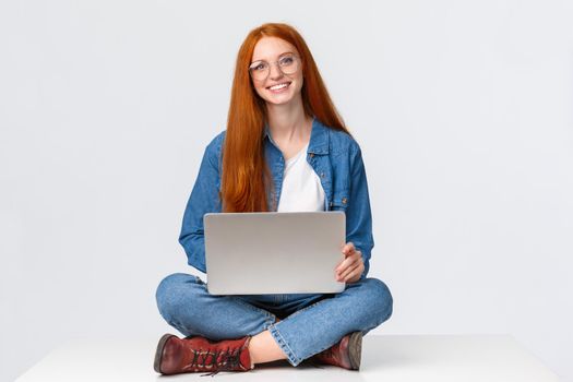 Attractive charismatic redhead caucasian female sit on floor with crossed legs, holding laptop laps, working on fresh air, writing new program, freelancing over white background.