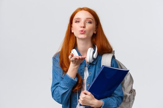 Lovely and tender, sensual redhead college girl, sassy student with red hairstyle, send air kiss, blowing mwah at camera passionately, holding backpack and folder with documents.