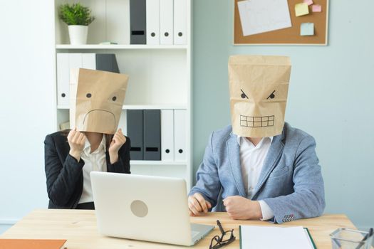 Business, emotions and people concept - Two angry and exhausted workers at working place. People wearing the packages on their heads with pictured emotions.