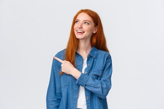 ,Dreamy carefree good-looking redhead european woman in denim shirt, looking pointing upper left corner, smiling delighted, making choice, seeing perfect product, recommend company service.