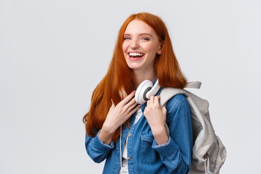 Education, student life and happiness concept. Cheerful good-looking redhead caucasian girl, college student with backpack and headphones over neck laughing smiling at camera.