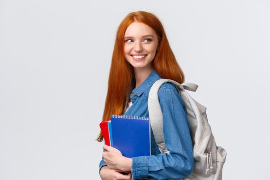 Girl seeing classmate in hall saying hi, turning back to greet someone, smiling joyfully, holding backpack and notebooks, heading back to class, studying in college, standing white background.