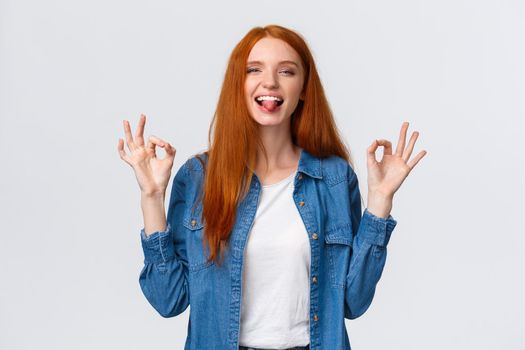Relaxed and carefree, positive redhead girl chilling on party, having fun leisure weekends, showing okay gestures calming down, assuring all good, showing tongue and smiling playful.